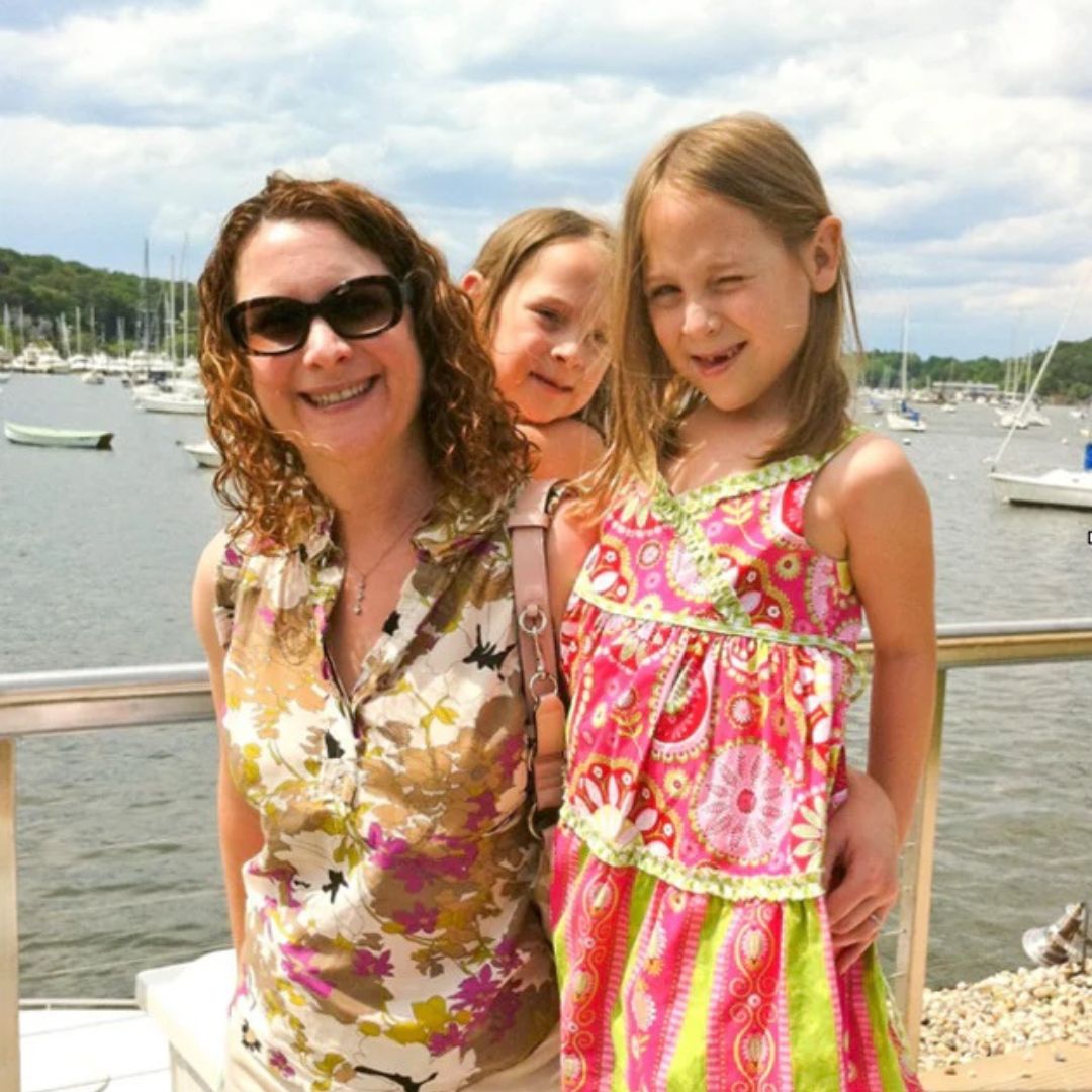 curly haired mom smiling next to her curly haired daughters in front of the pier