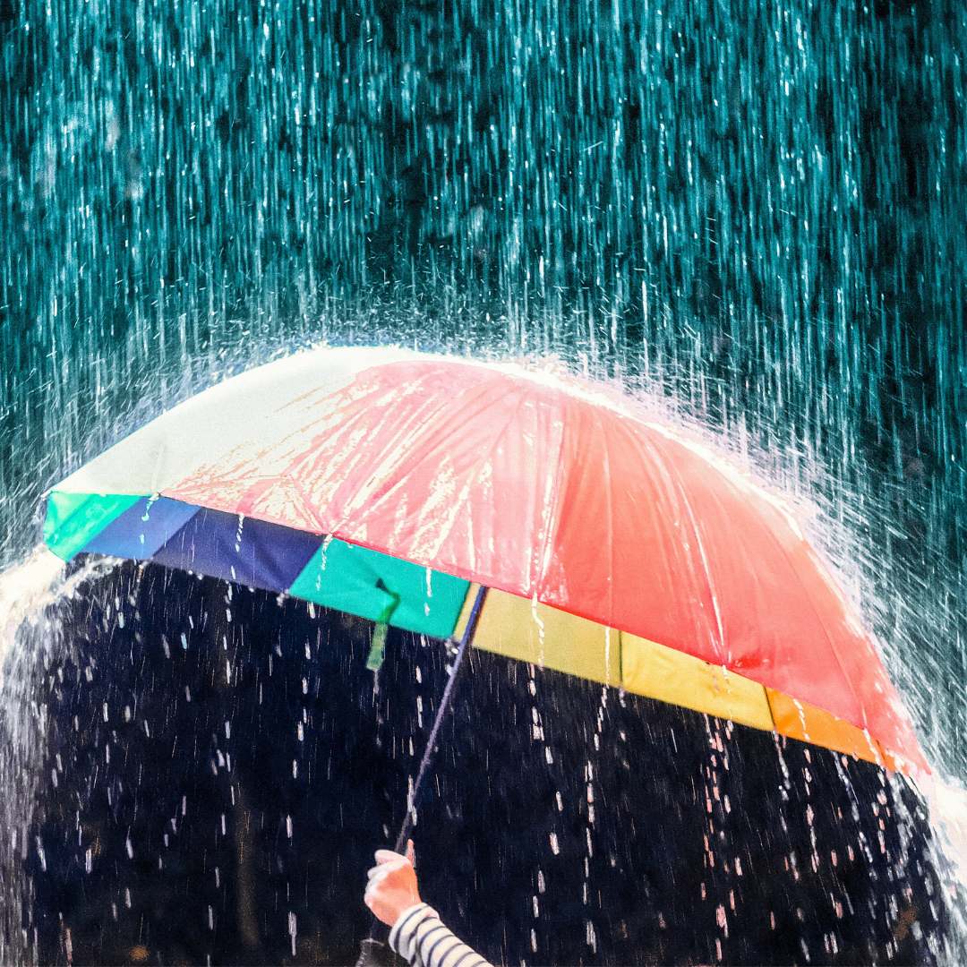 person holding a colorful umbrella out to disrupt the falling rain