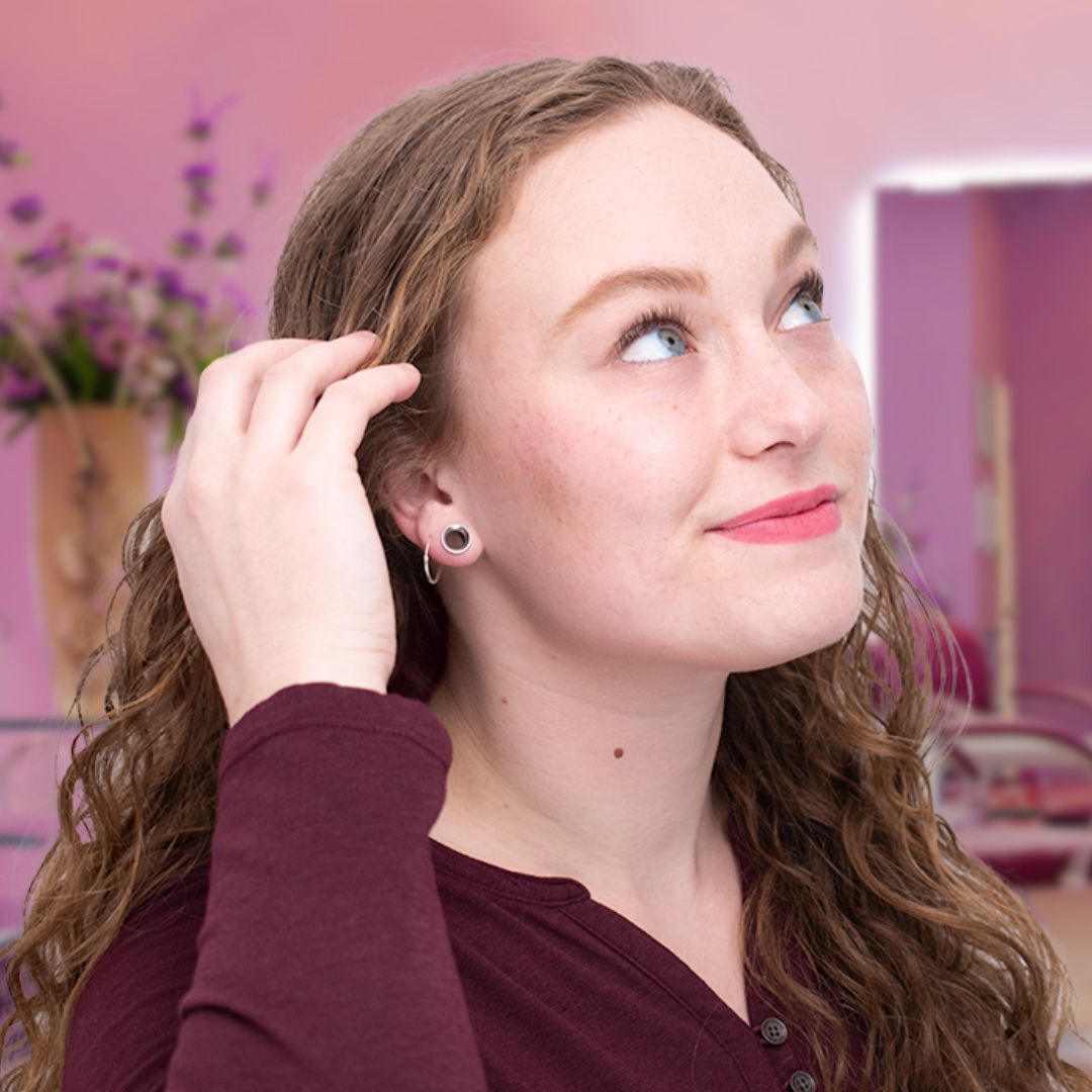 woman with curly hair smiling and looking up as she tucks her hair behind her ear