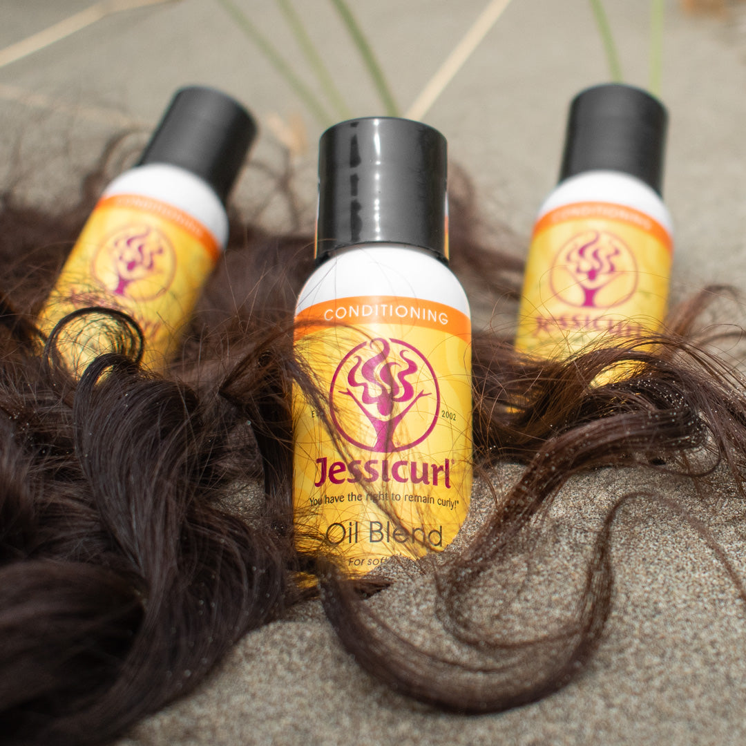 3 bottles of Oil Blend tucked into sand with ends of curly hair cascading around.