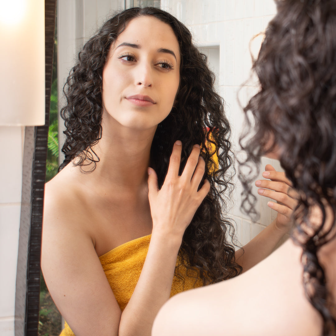 curly haired woman looking in the bathroom mirror, detangling her hair