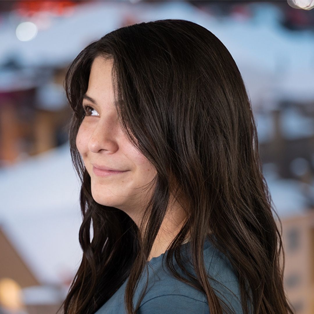 woman with brown wavy hair looking off into the distance with a snowy city hazily in the background