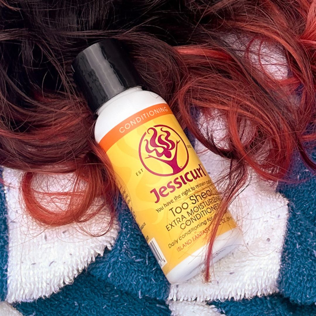 curly hair on a pool towel with a small bottle of Too Shea! Extra Moisturizing Conditioner laying on the hair