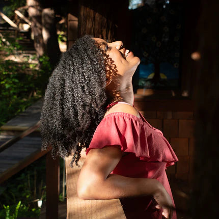 smiling curly haired woman leaning against the railing of a back porch and looking up into dappled sunlight