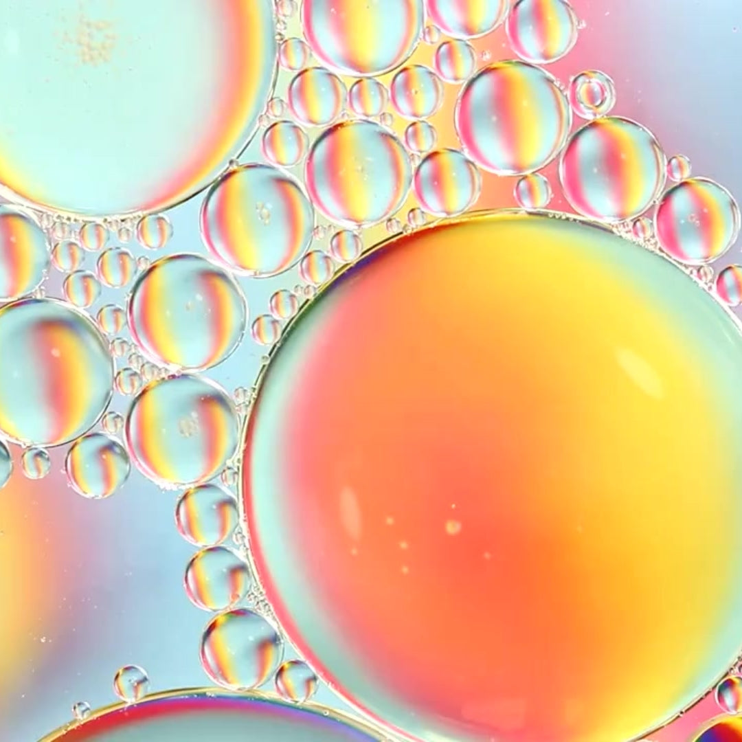 an extreme close up of soap bubbles gathered close and highlighted in yellows, oranges, pinks, and blues