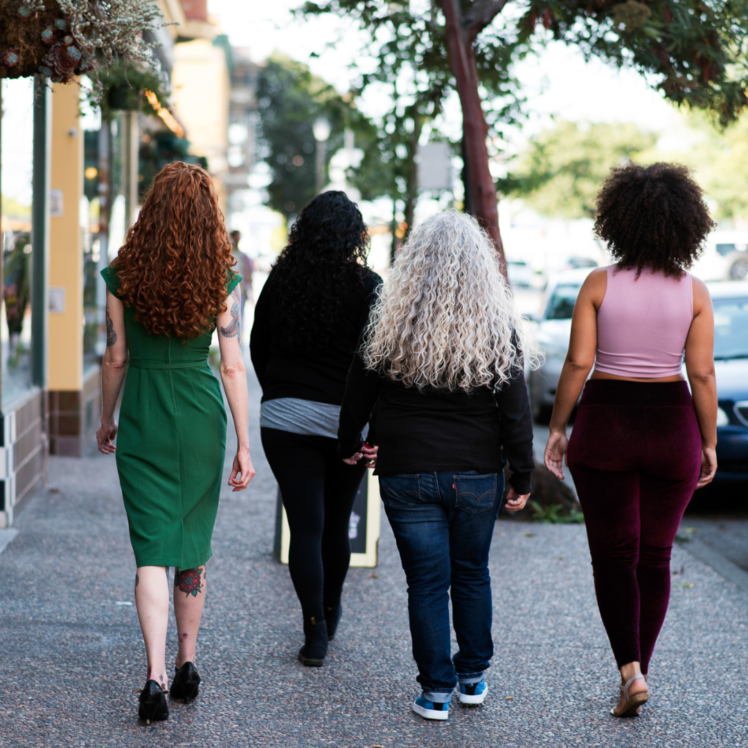 four curly haired women with different curl patterns walking away from the camera