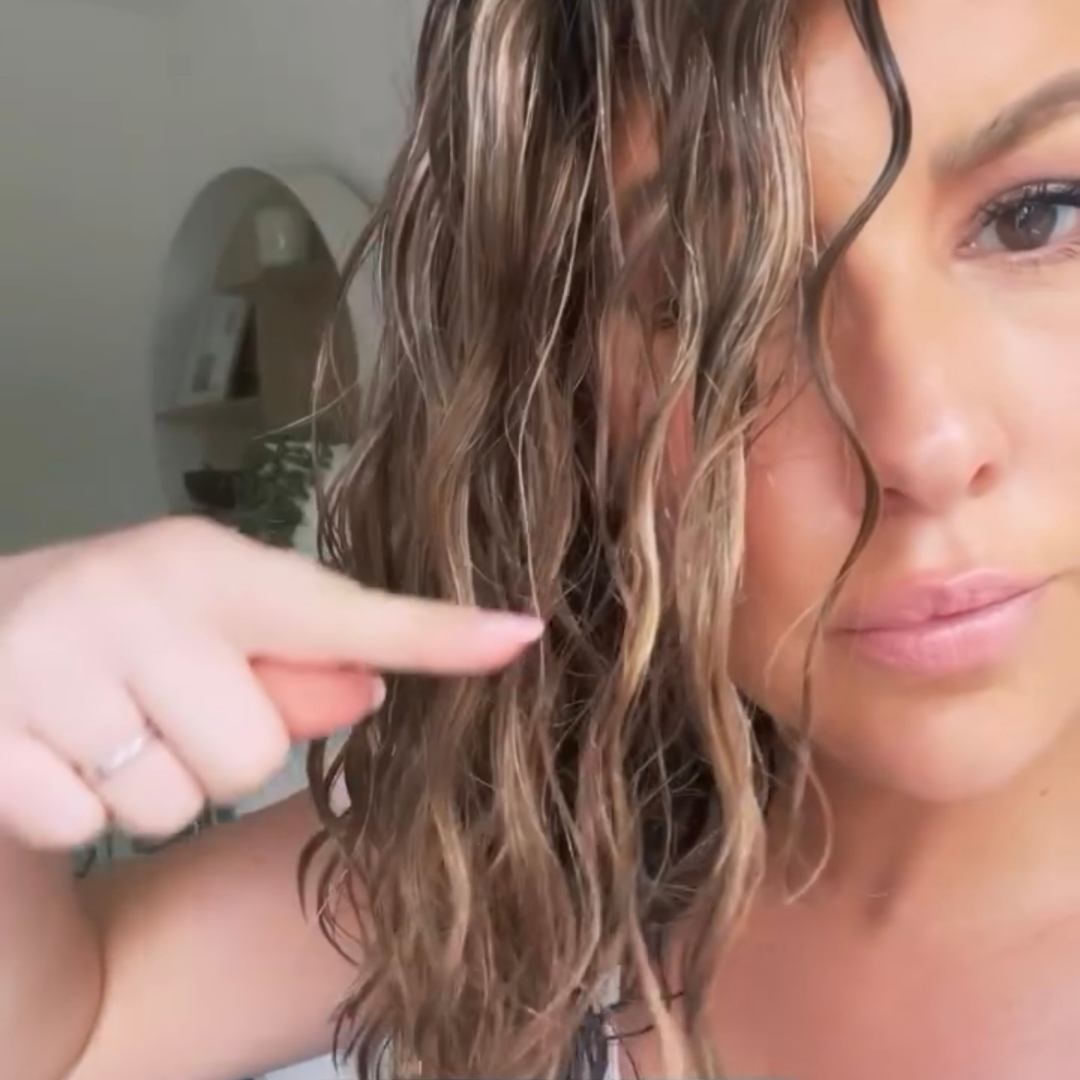 curly haire woman pointing out a piece of wet frizz in her hair
