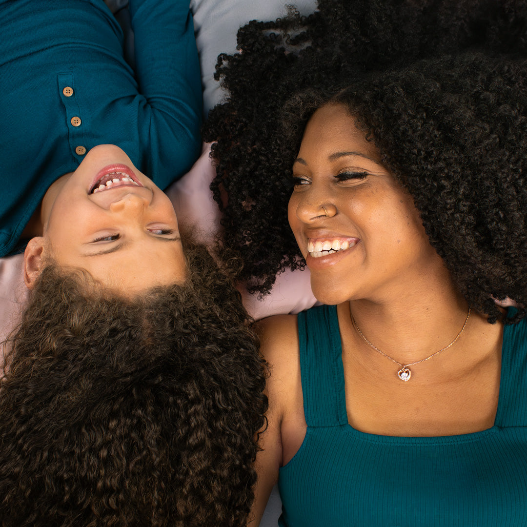 curl haired mother and young daughter laying in bed smiling at each other 