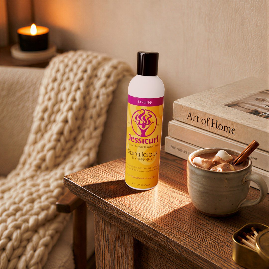 bottle of Jessicurl Spiralicious sitting on a side table next to a cup of cocoa and a stack of books with a cozy chair and blanket in the background