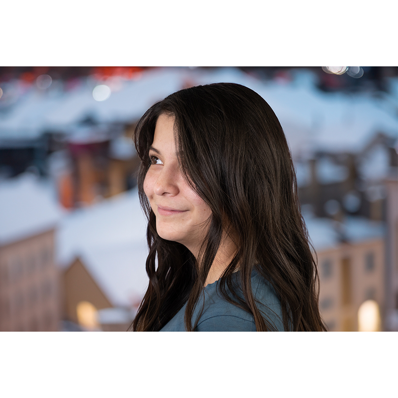 woman with brown wavy hair looking off into the distance with a snowy city hazily in the background