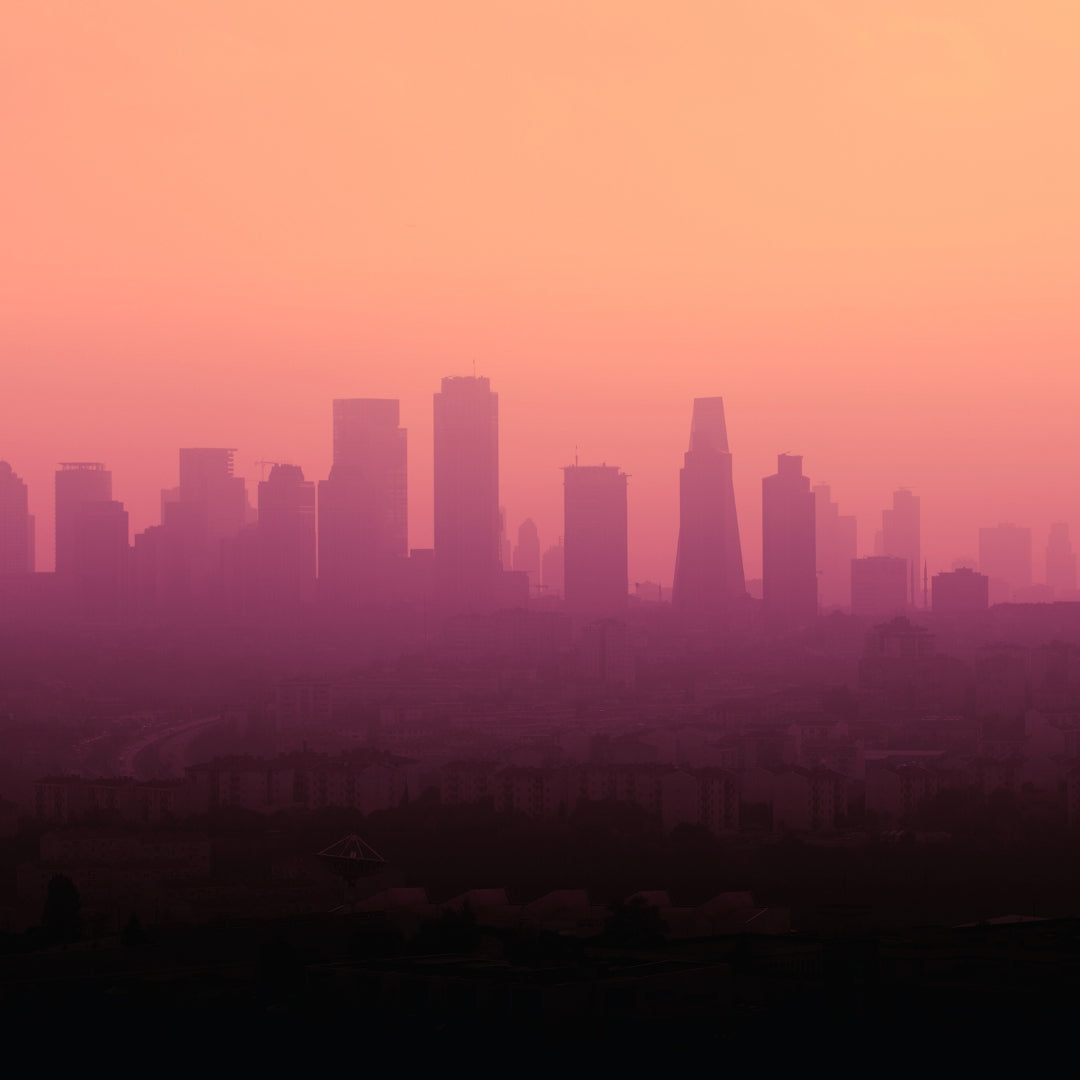 a city skyline just as dawn breaks, giving the sillouhette an orange-pink glow