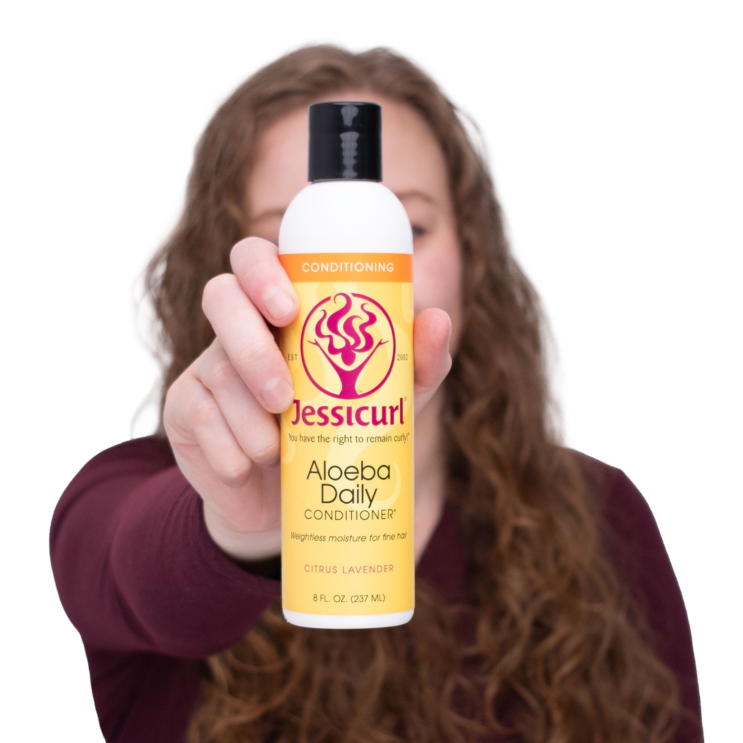 Woman with curly hair holding bottle of Aloeba Daily Conditioner out in front of her face.