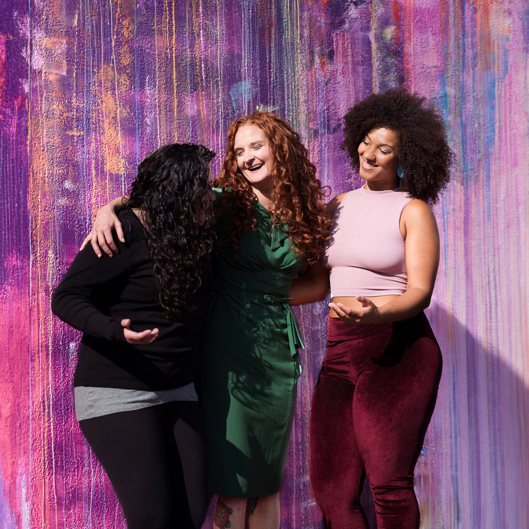 Jessica McGuinty with fellow curly women smiling together against a painted wall